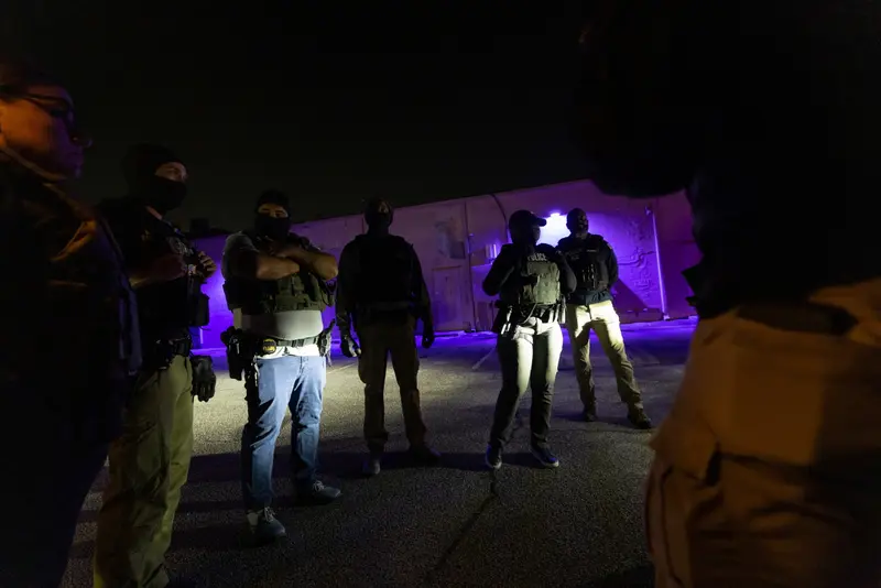 A group of officers standing in a parking lot at night wearing tactical vests and masks.