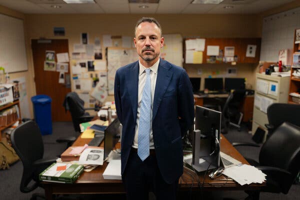 Joseph H. Thompson, a federal prosecutor, in a blue suit and light blue tie, stands near a desk.