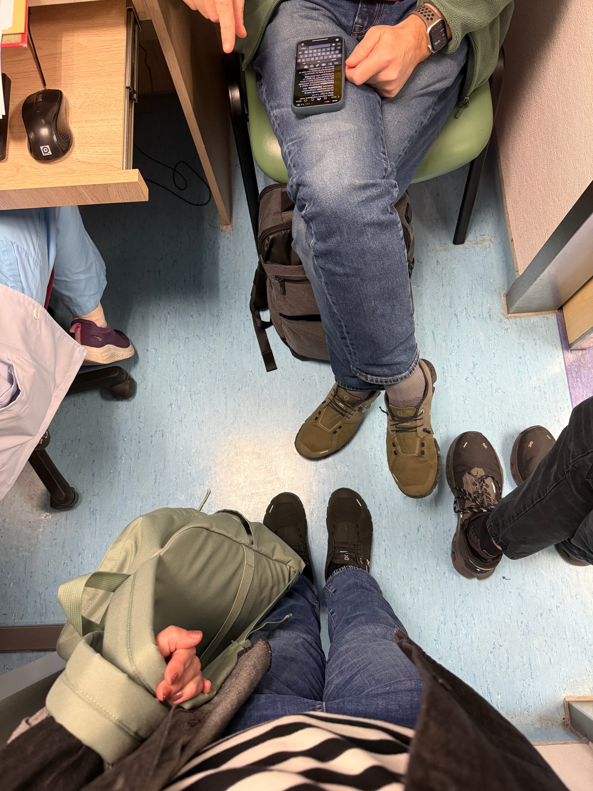 An overhead photo of four people’s feet standing on a blue linoleum hospital floor.