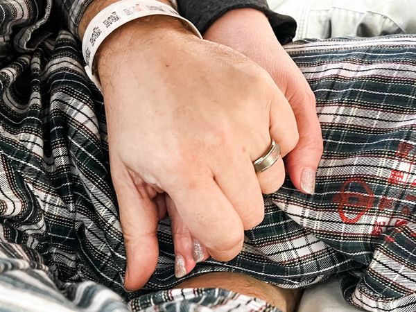A photo depicting two people holding hands over the plaid hospital pajamas provided to patients by the Hong Kong Hospital Authority.