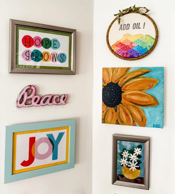 Six pieces of colorful art on a white wall. Text on the art: Hope Grows, Add Oil, Peace, Joy, and Here. 