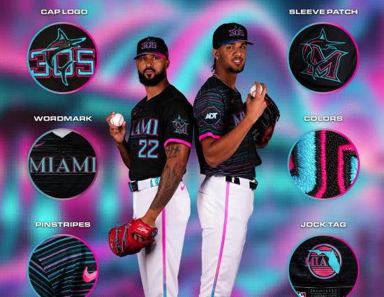 Two Marlins players in City Connect uniforms. Black jerseys with some faint pink and teal horizontal pinstripes and teal "Miami" and numbers on the jersey. White pans with hot pink stripes down the leg. 