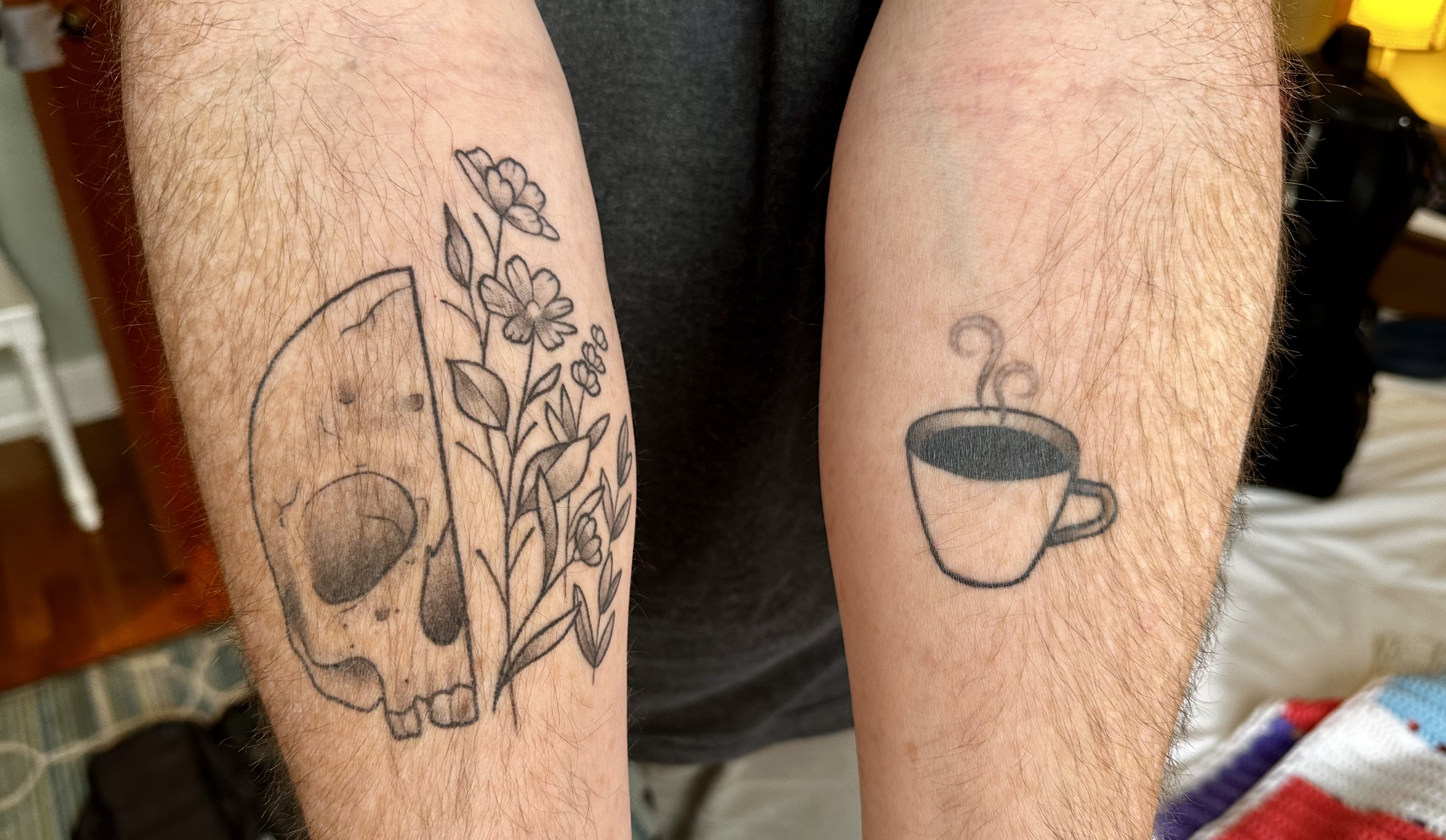 My two forearms, with one showing a coffee cup tattoo and the other showing a skull/flowers kind of thing