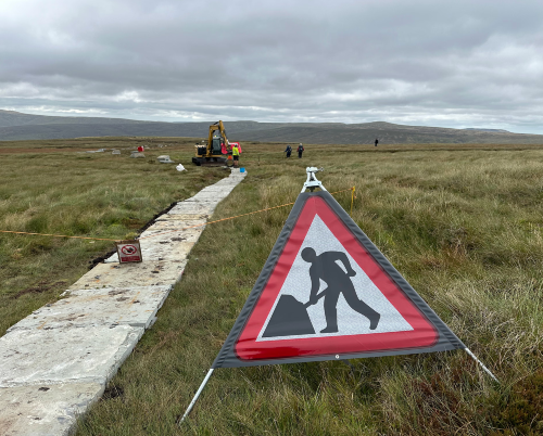 Slate walking slabs being placed over moorland by a construction crew
