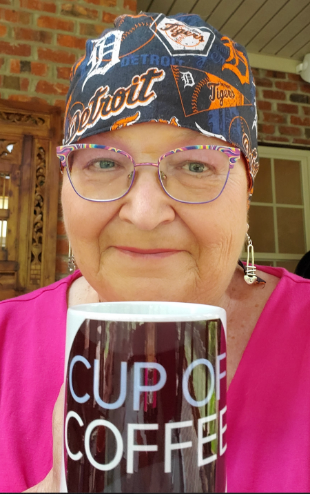 A woman in a pink shirt and beautiful rainbow glasses and a Detroit Tigers durag holdng a Cup of Coffee coffee mug