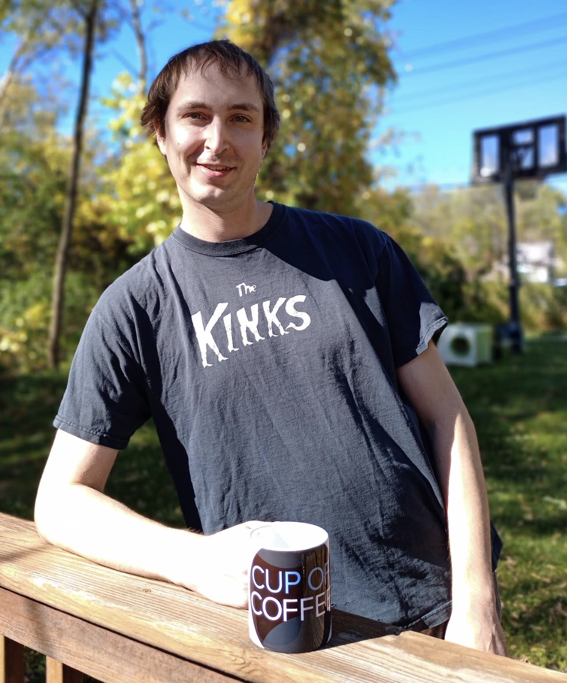 Subscriber David Hasbargen, posting outside on a deck, wearing a Kinks t-shirt, and holding a Cup of Coffee coffee mug