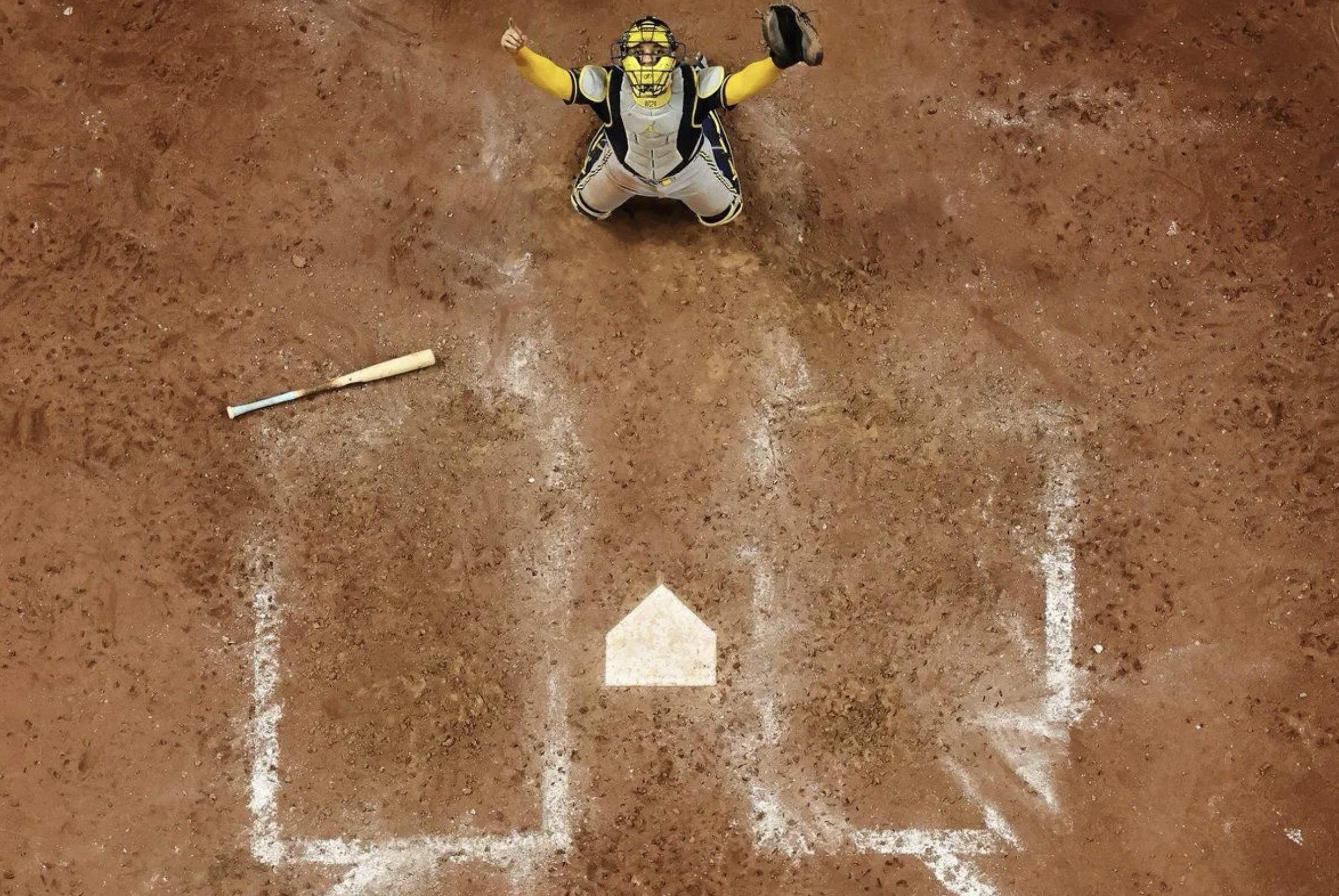Overhead shot of William Contreras catching the final out, his arms in the air, only the empty batter's boxes, home plate, and a bat on the ground in front of him