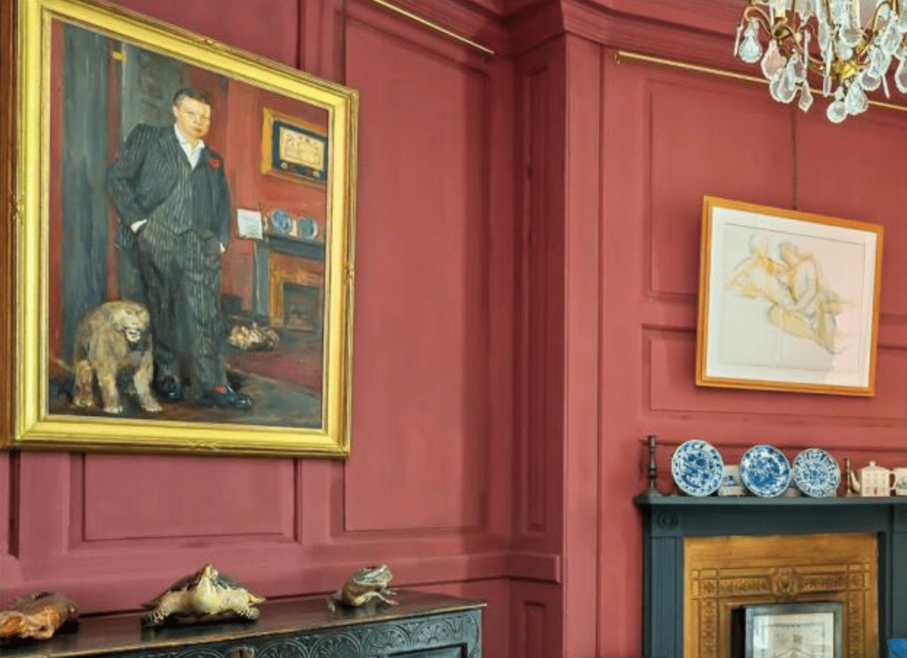 Painting of a young man in a suit next to what appears to be a baboon. Both of them are in front of a fireplace