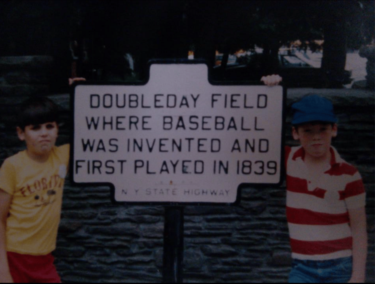 Photo of my brother and me from 1982 maybe in front of a sign at the Baseball Hall of Fame which says "Doubleday Field Where Baseball was Invented and First Played in 1839.