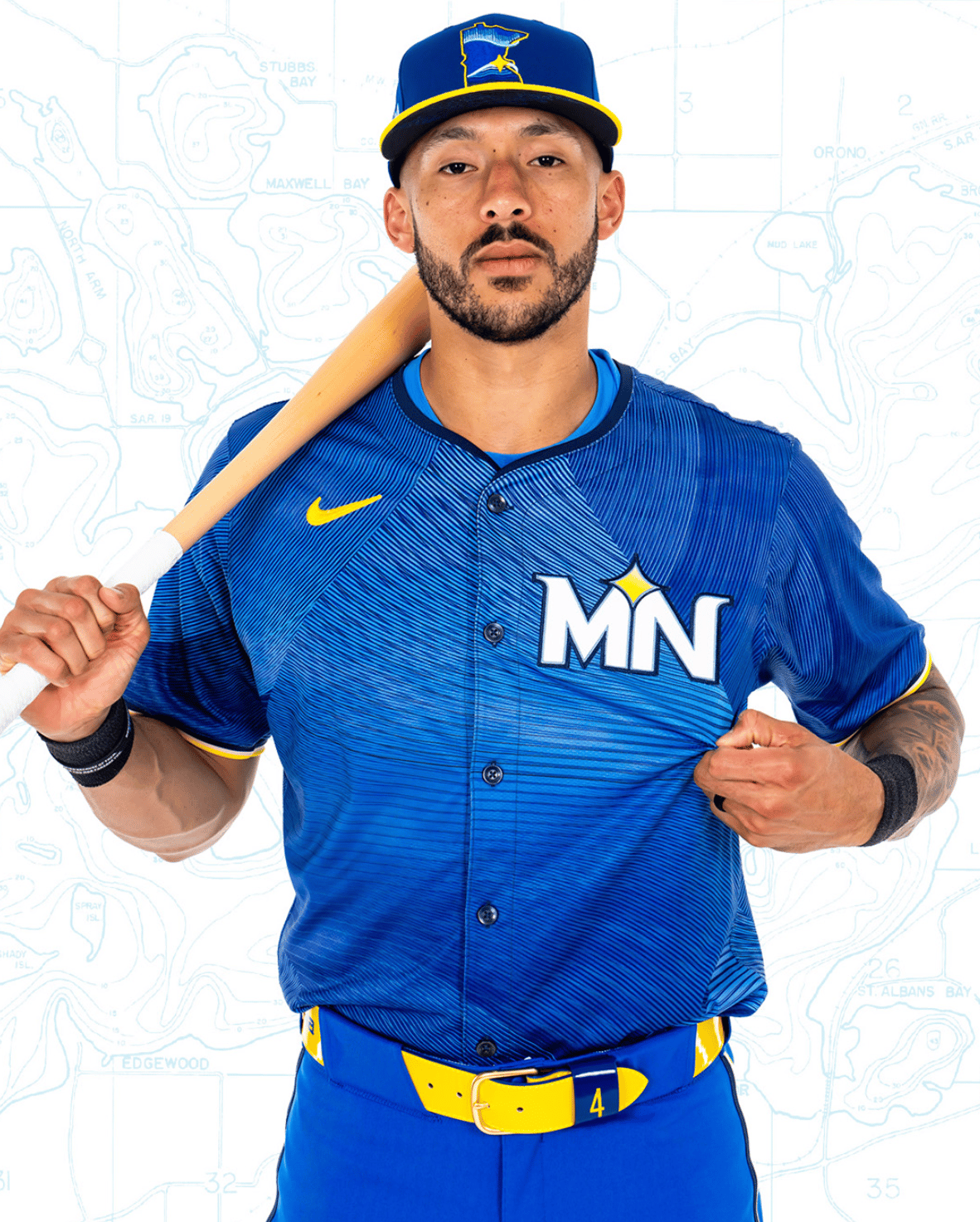 Carlos Correa in a royal blue uniform with "MN" on the chest and a yellow belt. Cap has the outline of the state of Minnesota