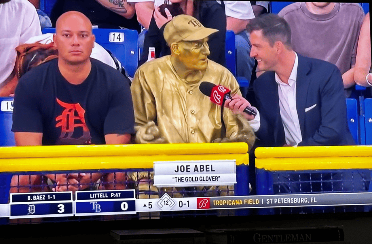 Two fans being interviewed in the stands. The one on the right has painted himslef gold from head to toe. The one on the left is just staring, dead eye, into the camera. 