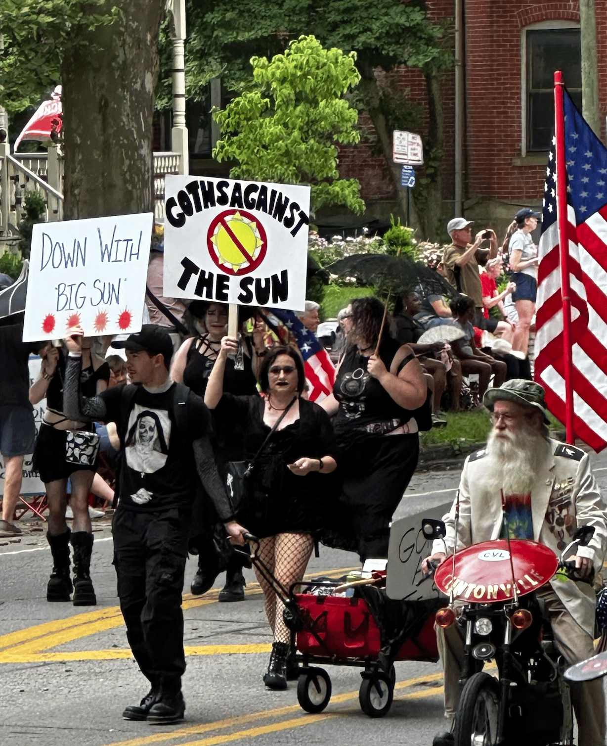 Goth parade marchers holding signs "down with big sun" and "Goths Against The Sun!"