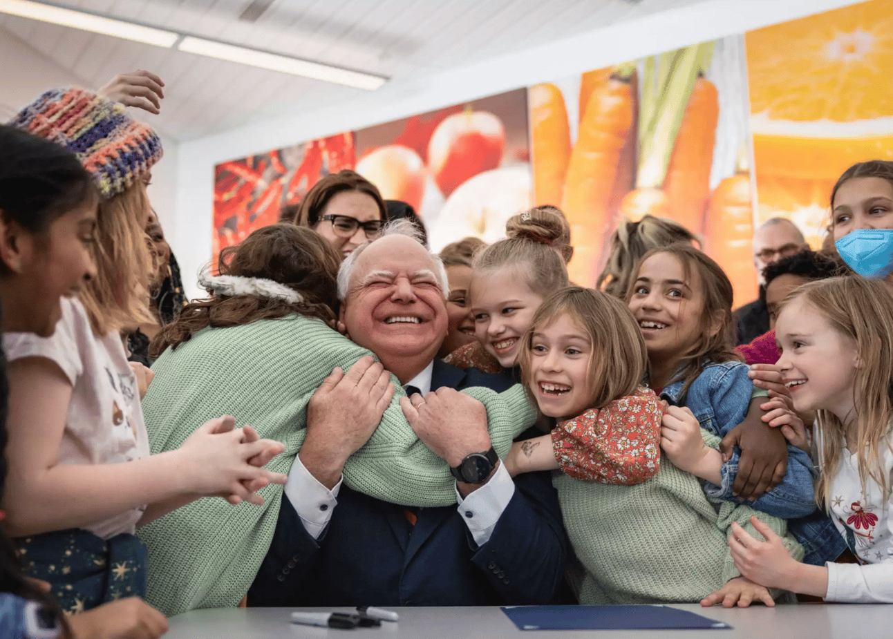 Tim Walz being hugged by kids after signing the school lunch bill into law