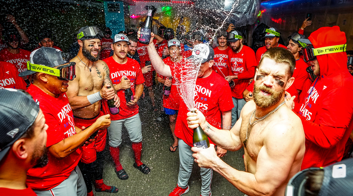 A shirtless Bryce Harper pops a champagne cork as he and other Phillies players celebrate their NL East title
