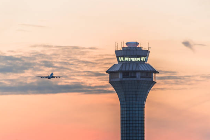 An air traffic control tower with an airplane taking off behind it. 