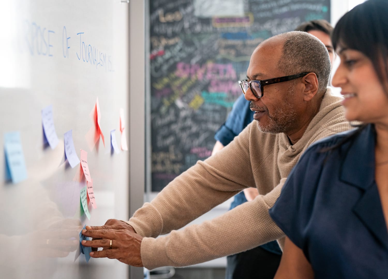 Kevin and Anika posting sticky notes on a white board.