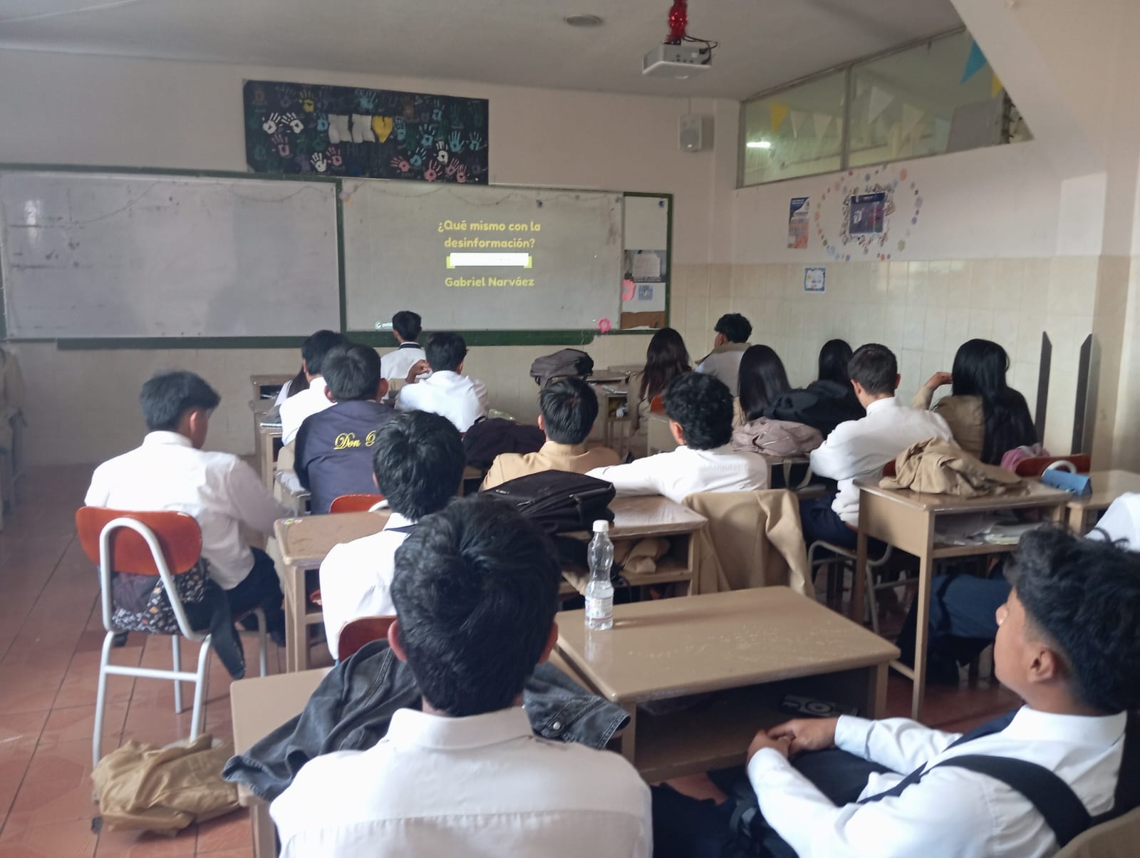 A classroom full of students sitting at their desks and looking at a white board with text on it.