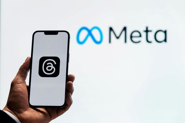 Meta logo on a phone in front of a white background that says "Meta"