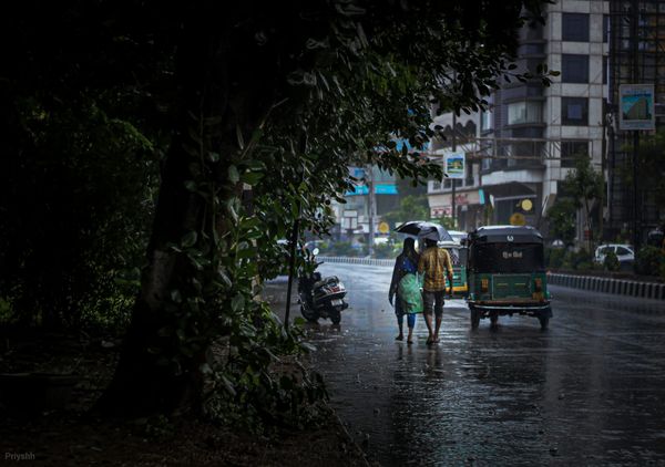 A couple waking down the street with an umbrella.