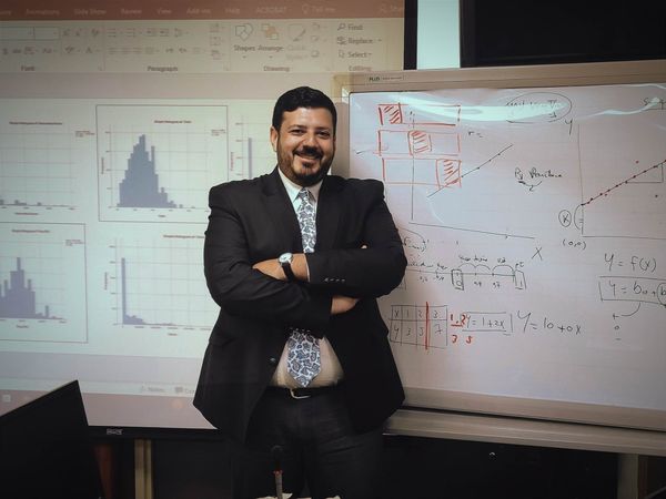 Eleraqi posing in front of a white board.