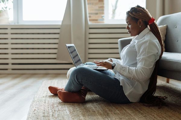 A woman sitting on the floor and working on her laptop. 