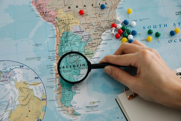 A map of Latin America and a person holding a magnifying glass over Argentina.