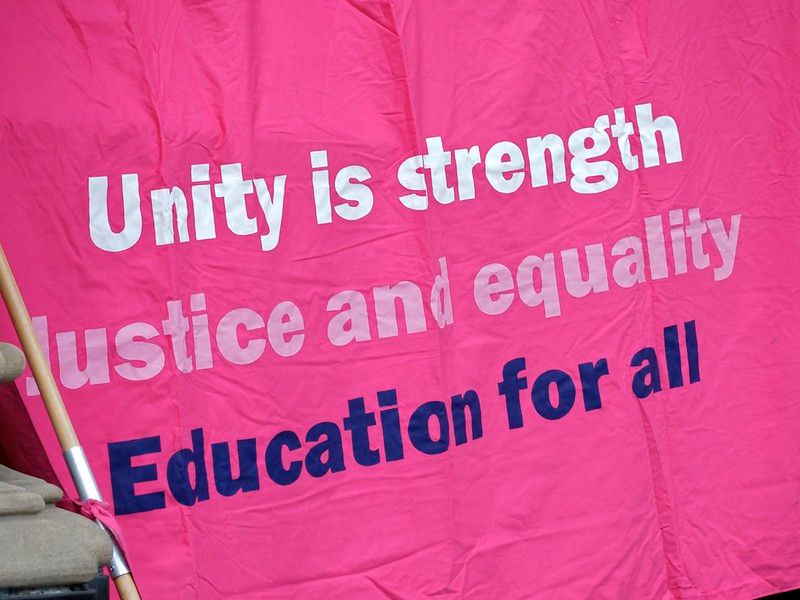 Bright pink banner with the slogan "Unity is strength, Justice and equality, Education for all'