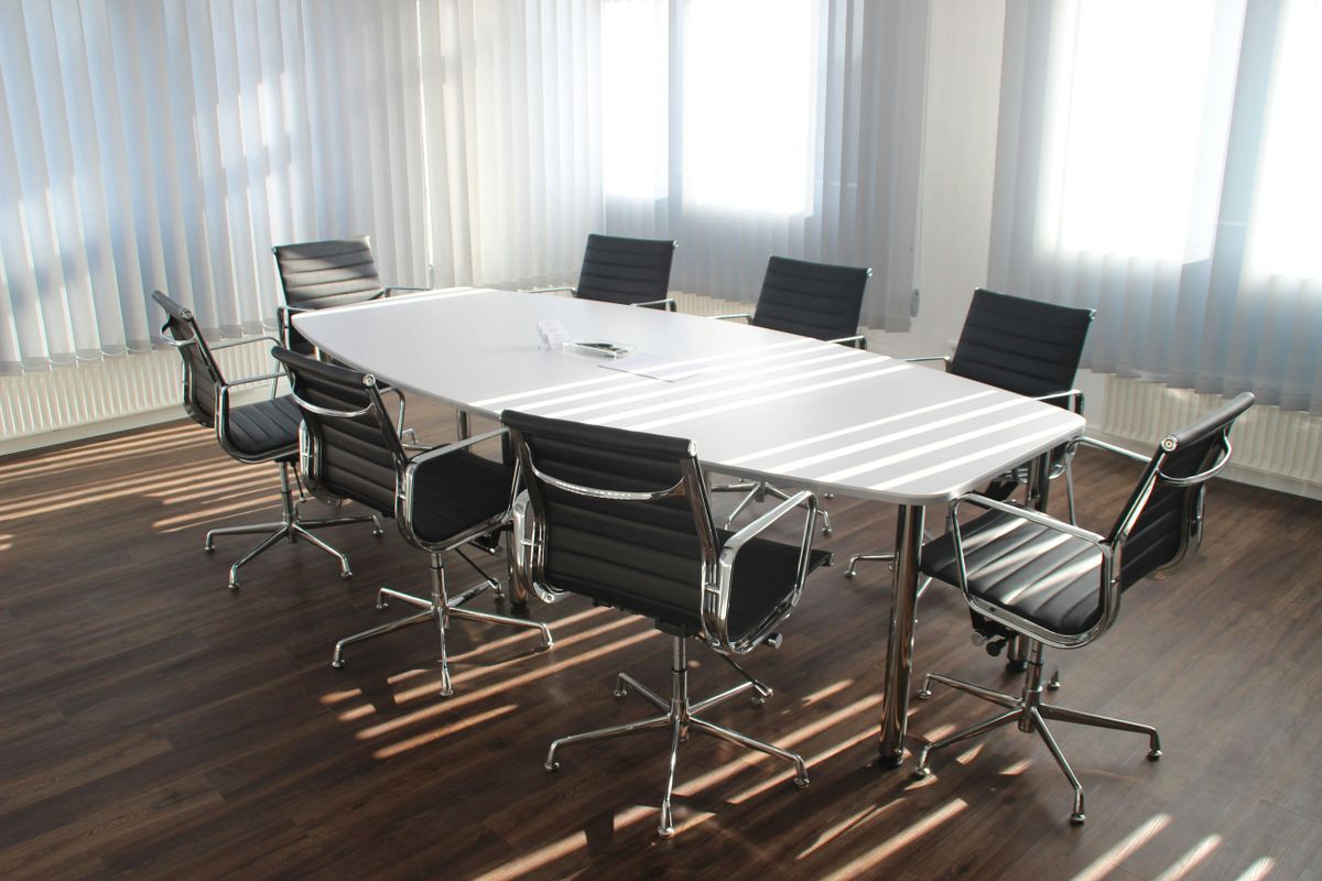 A meeting room with a white rectangular table, surrounded by eight black office chairs