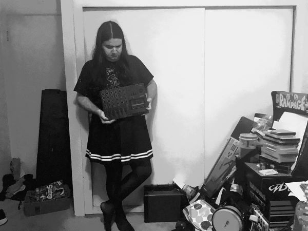 a person named Rose stands holding a small synth in her room. around her are bongos, a Rampage arcade cabinet, and more. 