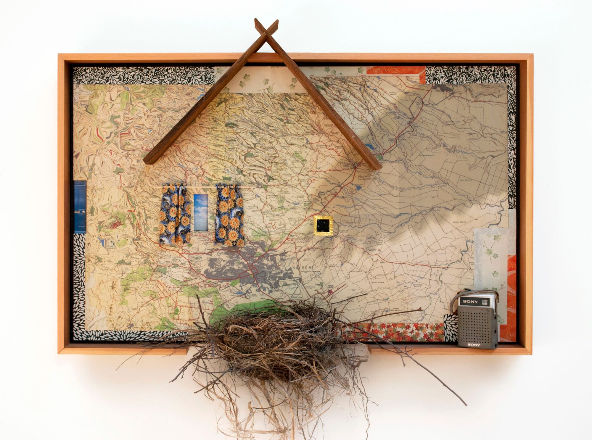 A mixed media collage of reprinted maps of Kenya, collected papers, fabric scraps, chocolate wrappers, a bluejay nest, cedar shingles, AM radio
