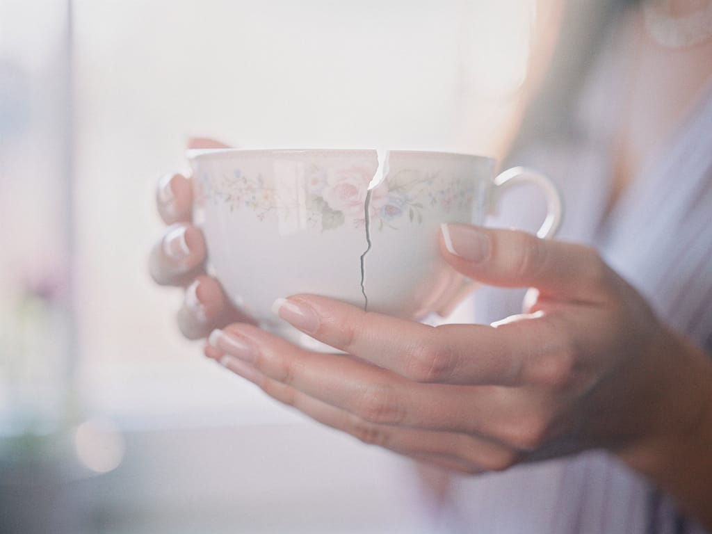 A cracked porcelain teacup held carefully, symbolizing fragile well-being