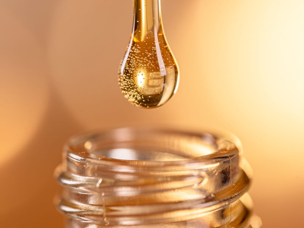 Golden serum droplet falling from a glass dropper