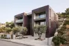 Hillside residence with deep aubergine ribbed ceramic facade panels, exposed concrete balcony recesses and olive trees.