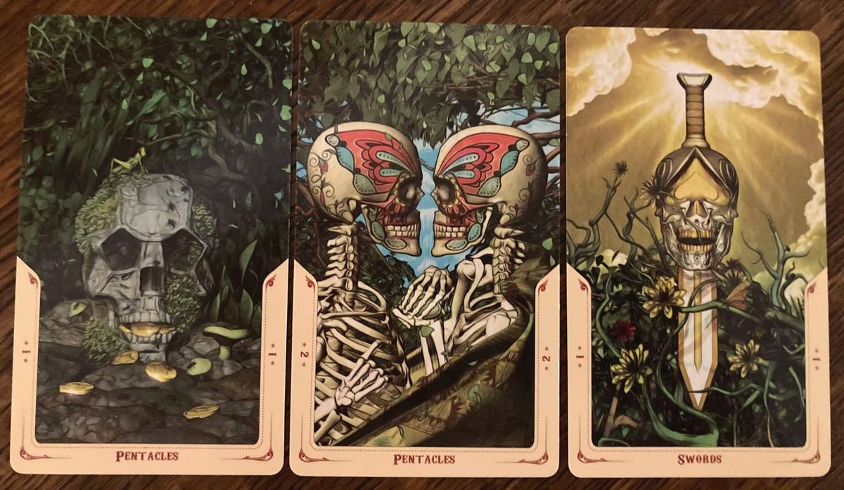 3 cards in a row from the Santa Muerte Tarot, which has a visual theme of skulls and skeletons. Ace of Pentacles, 2 of Pentacles, Ace of Swords.