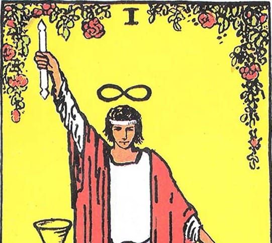 The Magician wears a red robe and has an infinity sign above his head. He holds one arm up, with a wand, and one down. The upper edge of the image has a border of roses.
