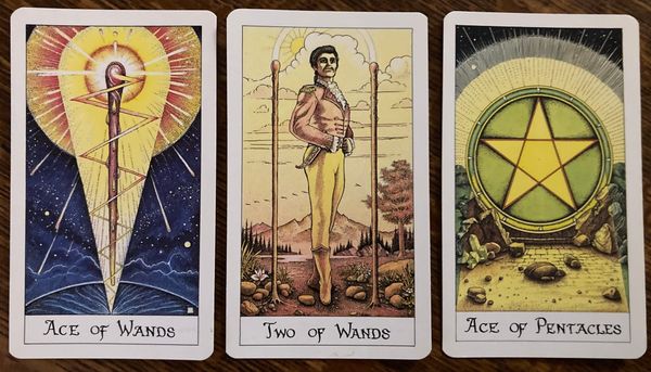 Three cards from the Cosmic Tarot deck: Ace of Wands, 2 of Wands, and Ace of Pentacles.