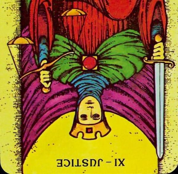Upside-down, a crowned figure sits holding an upright sword in one hand and a tipped scale in the other.