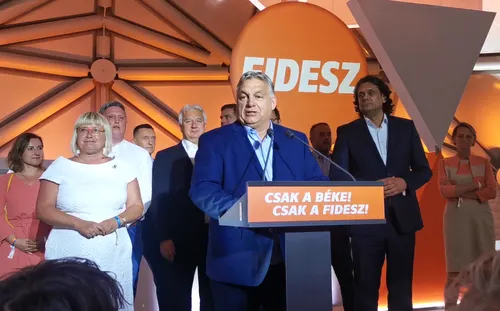 Viktor Orbán mentre parla con enfasi dietro un podio durante un comizio politico in Ungheria, circondato da diverse bandiere nazionali ungheresi.