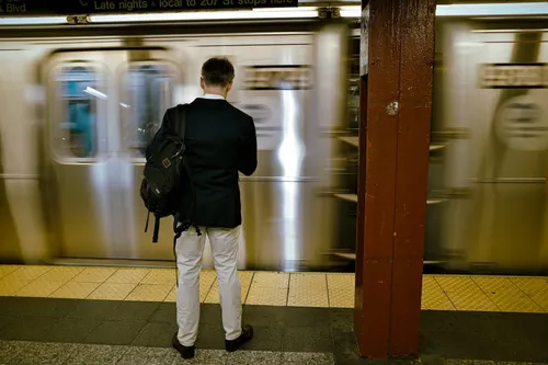 Uomo di splle con abiti da impiegato e zaino su una spalla che attende che si aprano le porte del vagone della metropolitana