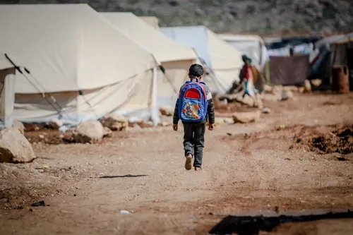 Un bambino, con uno zaino sulle spalle, cammina in un campo profughi a Idlib, in Siria.