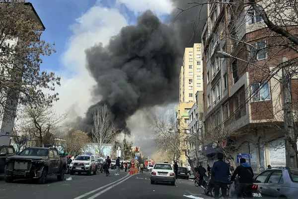 Vista di una strada di una città iraniana con colonna di grande fumo, con persone in auto e a piedi che vivono la quotidianità. 