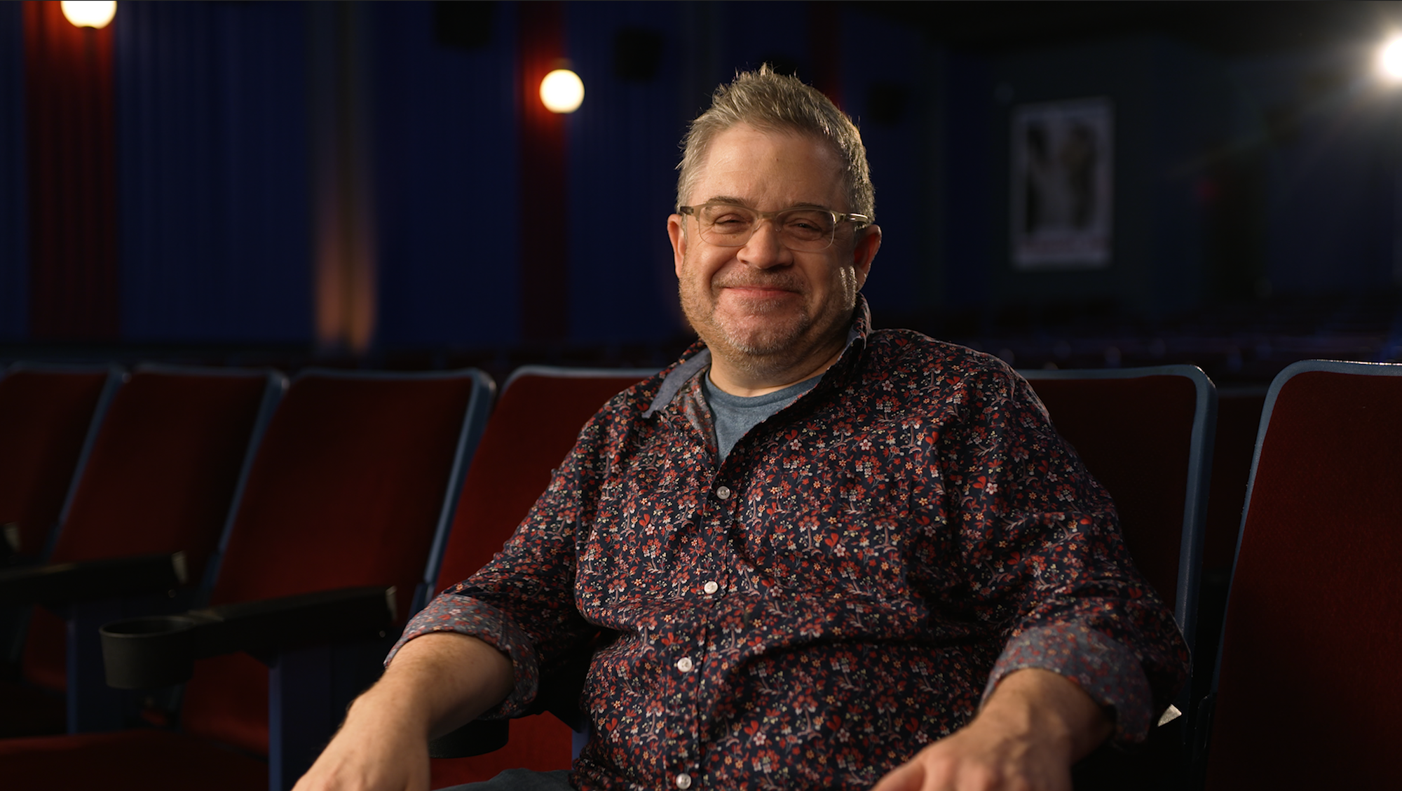 photograph of Patton Oswalt sitting in a movie theater alone
