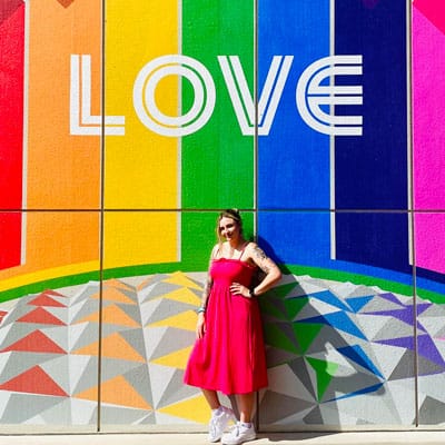 "LOVE"라고 적힌 무지개 벽화가 있는 건물 앞에 서 있는 Adele의 사진