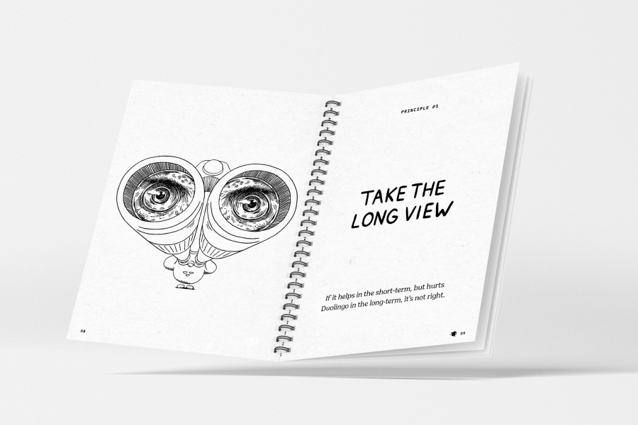 An open spiral bound book. The left page has a sketchy illustration of Duo using binoculars. The right page has the words "Take the long view. If it helps in the short-term, but hurts Duolingo in the long-term, it's not right."