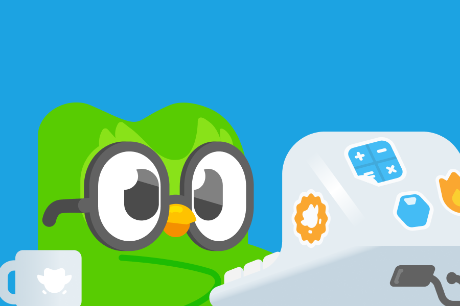 Duo wearing glasses at a desktop computer with Duolingo stickers on it. 