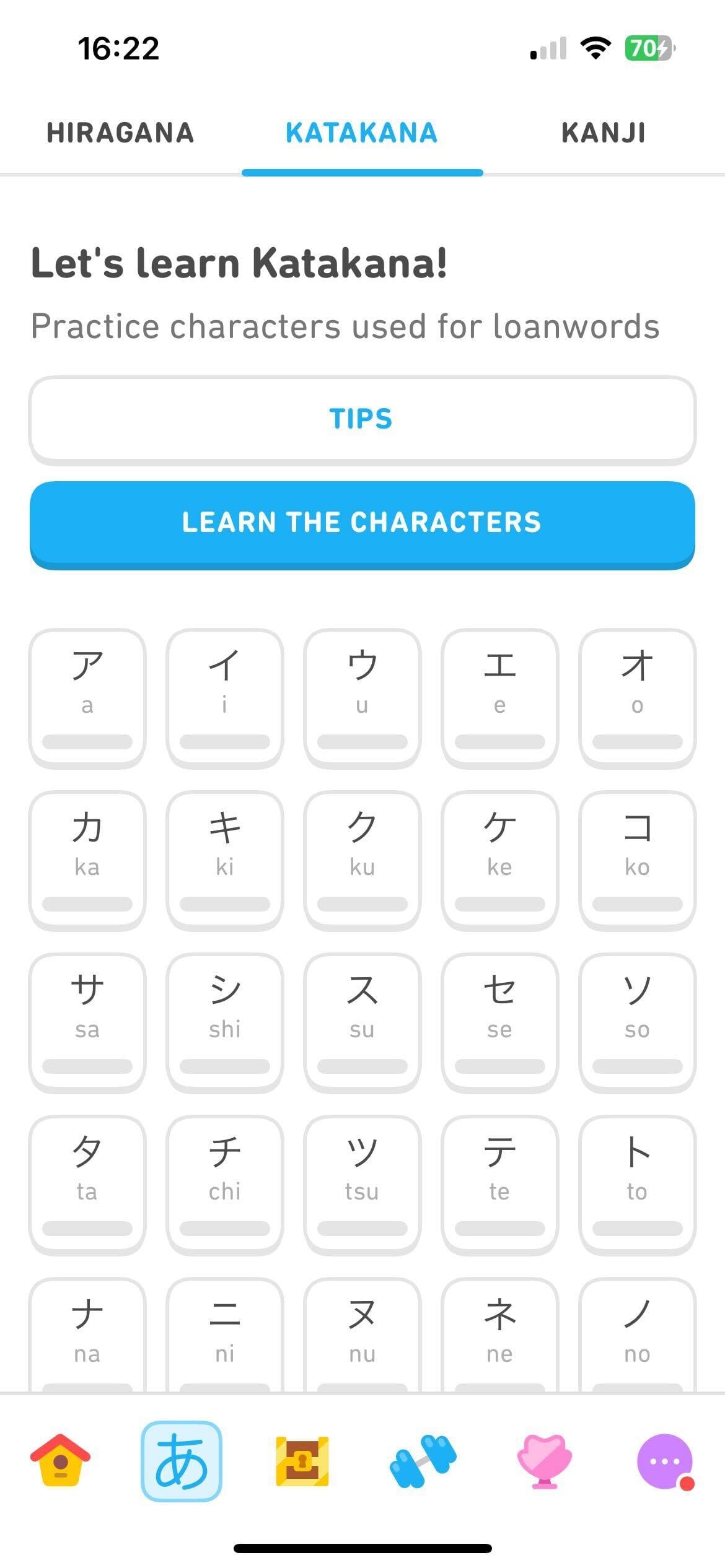 Captura de tela da aba de prática dos sistemas de escrita no curso de japonês para falantes de inglês. Na parte de cima, há o texto “Vamos aprender katakana! Conheça os caracteres usados em palavras que vieram de outros idiomas”. Em seguida, há o botão “Dicas” e o botão “Aprender os caracteres”. A maior parte da tela mostra uma tabela de 5 linhas e 5 colunas, na qual há blocos com diferentes caracteres do katakana e letras do alfabeto latino representando o som de cada um. Mais blocos vão aparecer se a tela for rolada para baixo.