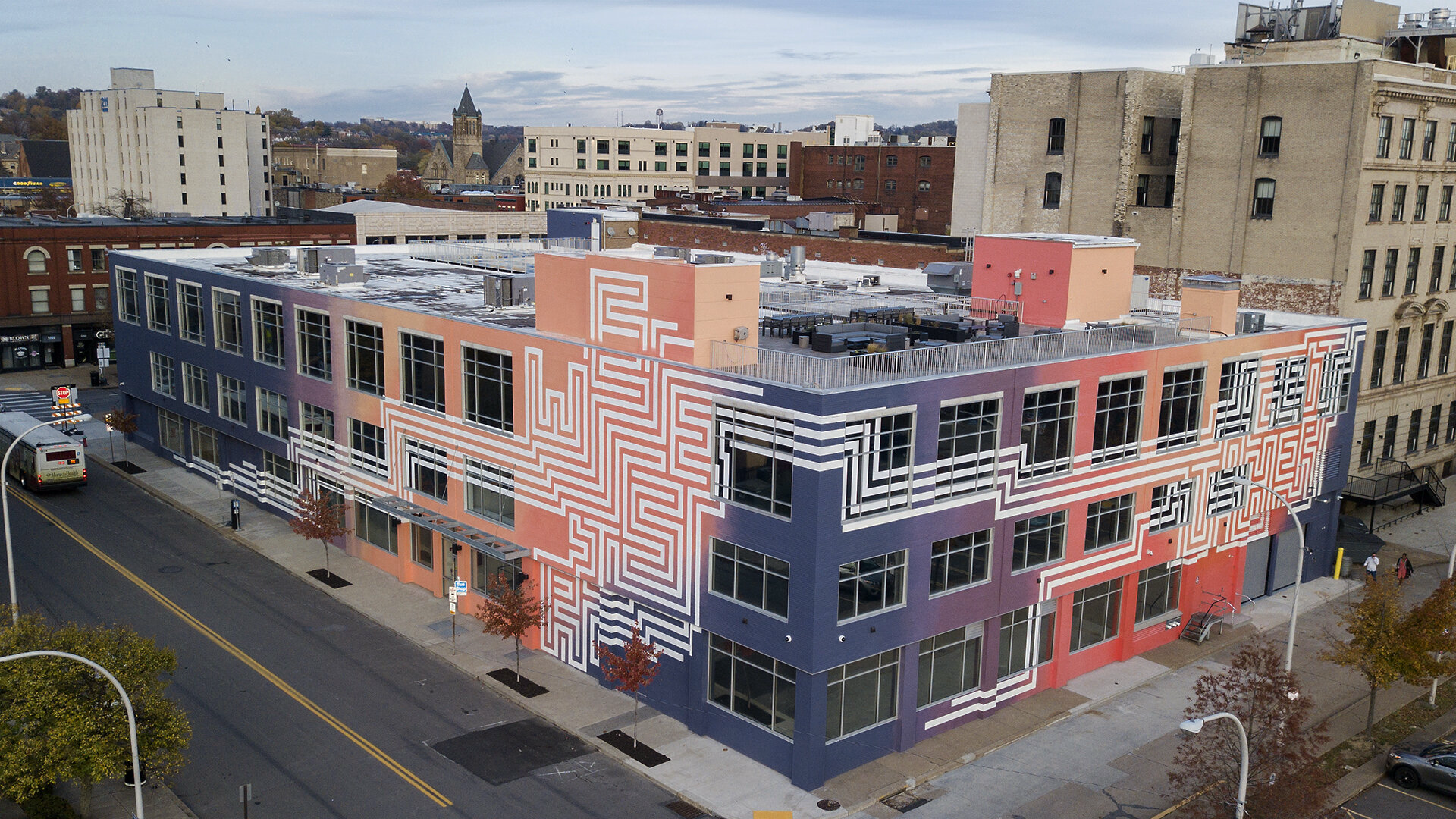 Aerial photograph of Duolingo's East Liberty headquarters. The building is covered in a mural of warm colors with maze-like white writing that reads “We rise” on one side of the building and “together” on the adjoining side.