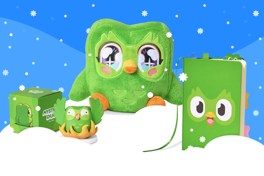 Un peluche anime de Duo, un cuaderno de Duolingo y una caja sorpresa con una figura de Duolingo sobre nieve