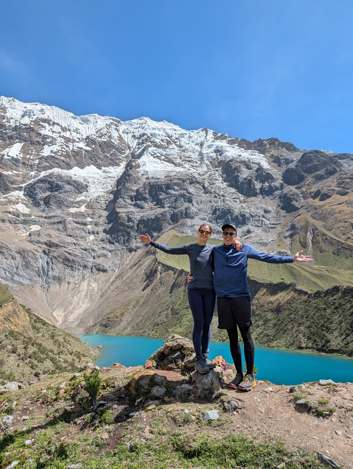 Natalie and her husband standing in front of Humantay Lake with their arms outstretched.