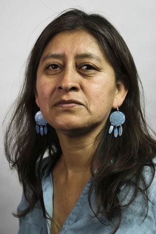 힐라리아 크루즈 박사의 사진. 그녀는 카메라를 바라보고 약간 미소를 짓고 있다. 그녀는 길고 웨이브 있는 짙은 색 머리를 가지고 있으며, 크고 연한 파란색 귀걸이를 하고 있다. 귀걸이는 큰 원과 그 아래에 세 개의 작은 타원형이 매달려 있는 모양이다.